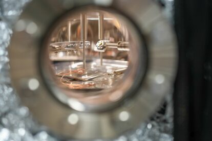Ein rundes Sichtfenster gibt den Blick ins Innere eines Rastertunnelmikroskops frei, wo verschiedene Maschinenteile aus Edelstahl erkennbar sind.